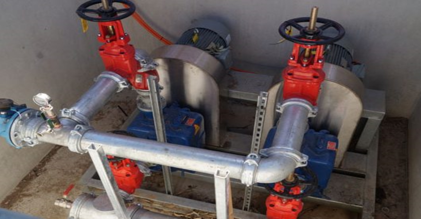 Duplex Hydroprime self-priming trash pump system with red isolation valves and galvanized piping, installed for wastewater management at a large-scale chicken farm operation