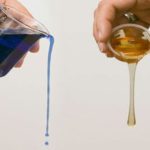 Two hands holding a glass filled with blue liquid, creating a visuall illustration of fluid viscosity