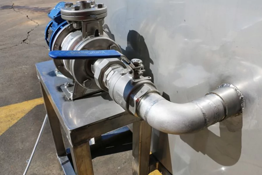 Close-up of a stainless steel outlet valve and pipe assembly mounted on a tank, with a blue-handled ball valve for flow control.