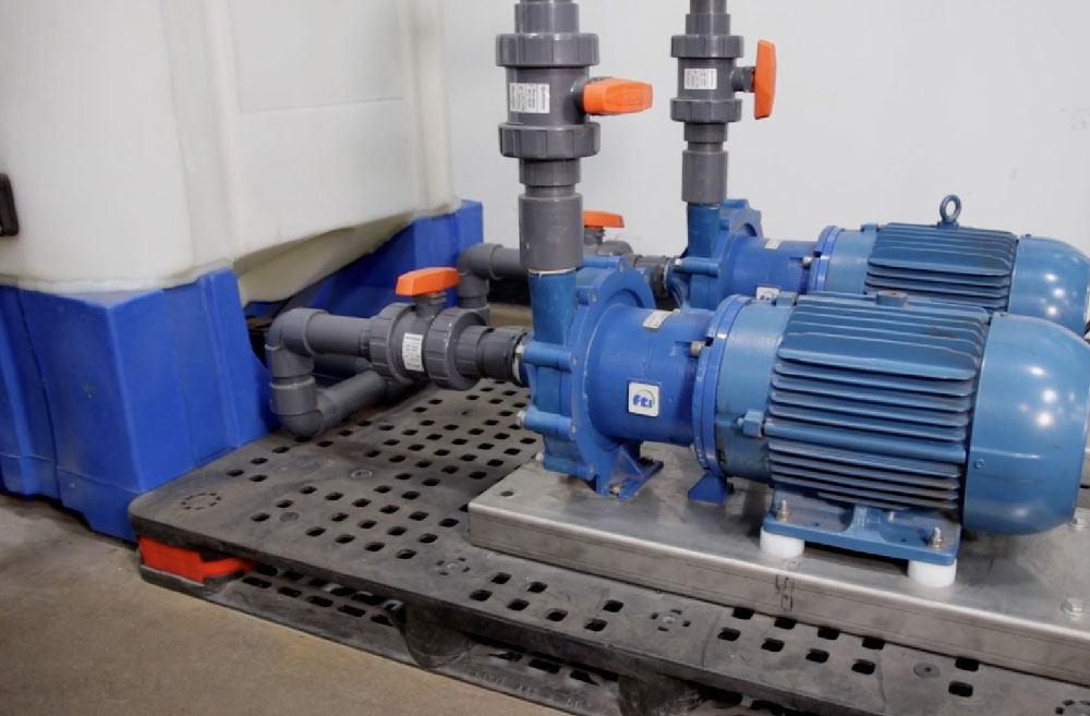 Dual Finish Thompson Inc. (FTI) magnetic drive pumps connected to PVC pipework beside a chemical storage tank. Optimized for chemical dosing, recirculation, and transfer of hazardous fluids in industrial operations.