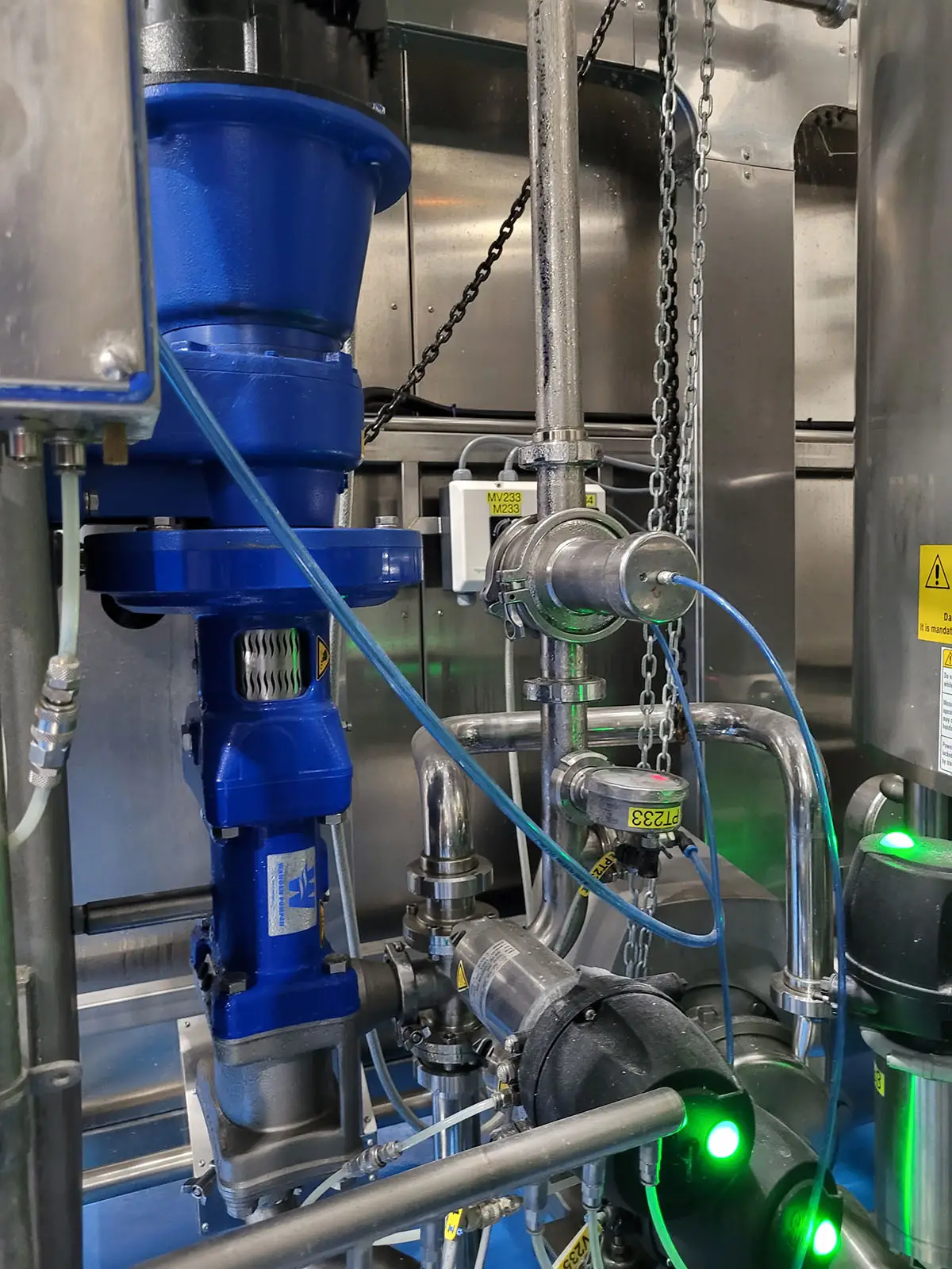 Close-up of a blue Wangen twin screw pump operating within a stainless steel processing system, used for gentle and sanitary transfer of high-viscosity products like bakery batter or food products