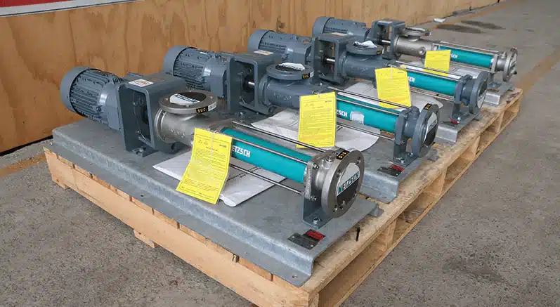 Four NETZSCH positive displacement pumps with electric motors and stainless steel housings arranged on wooden pallets. Engineered for precise and reliable transfer of slurries, polymers, and chemicals in manufacturing and wastewater industries.