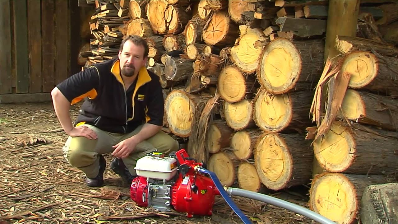 Technician showcasing a portable red Davey water transfer pump with a petrol engine near a stack of firewood. Ideal for agricultural, irrigation, and emergency water transfer applications in rural or commercial settings.