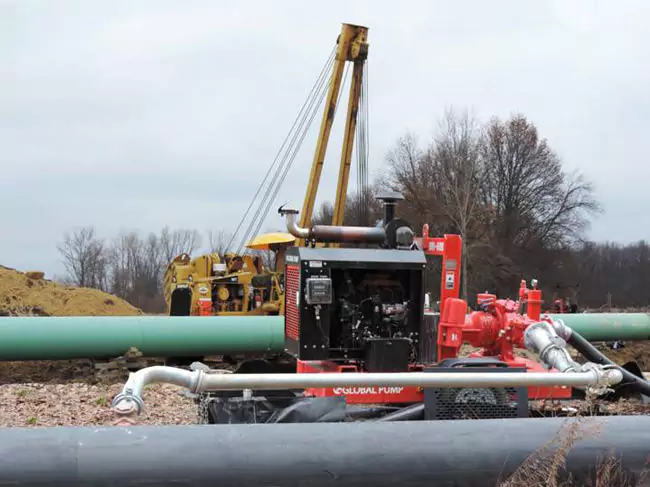 Global Pump GSC Wellpoint system at a pipeline construction site. The red centrifugal pump is managing groundwater control while large green pipes are being installed by heavy machinery.