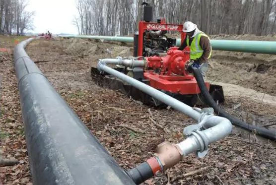 Global Pump GSC Wellpoint centrifugal pump used for trench dewatering. A worker monitors the hose connections as the red pump system removes groundwater along a pipeline project.