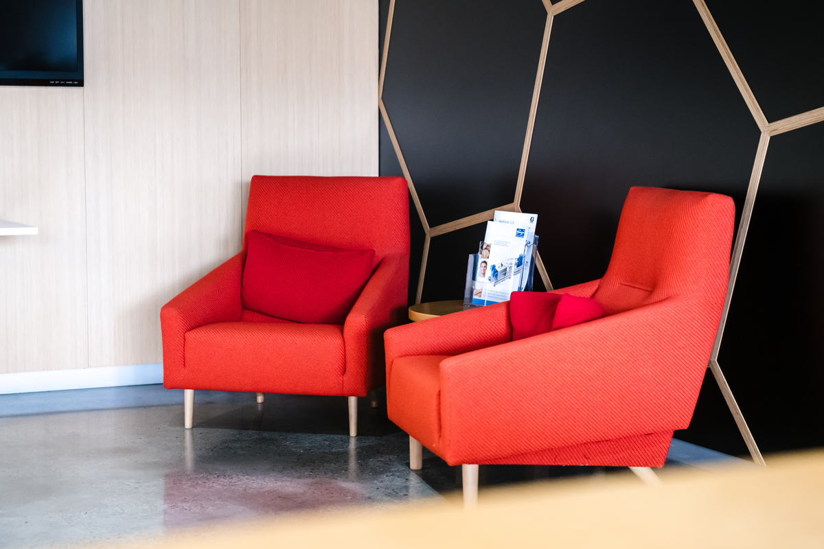 Bright, modern office lounge with two red armchairs, a side table, and brochures in a stylish waiting area.
