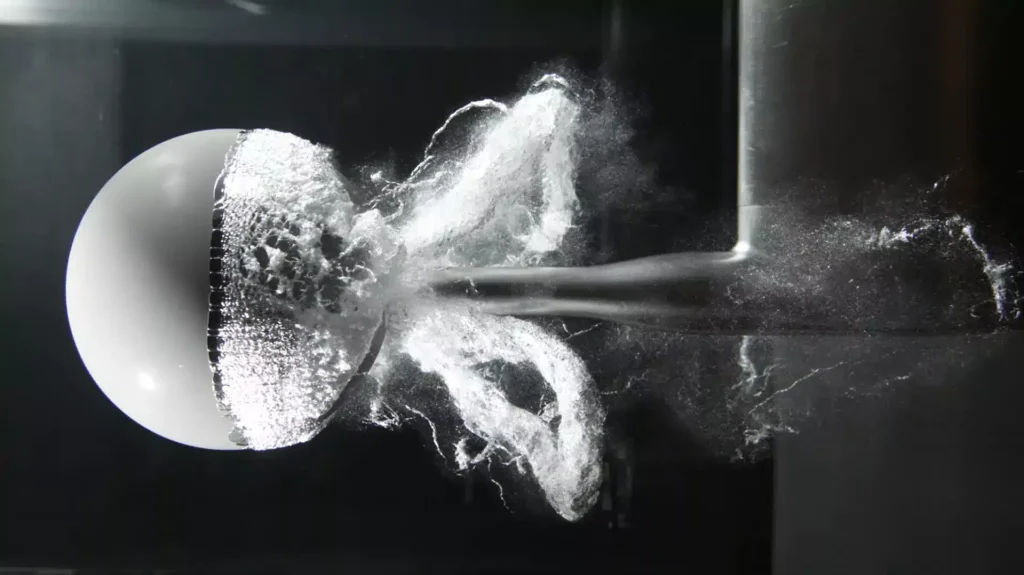 High-speed photography showing the destructive collapse of vapor bubbles (cavitation) around a submerged spherical object, illustrating the physical phenomenon that damages industrial pumps and impellers